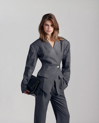 Woman wearing a gray pinstripe suit holding a black clutch against a light gray background